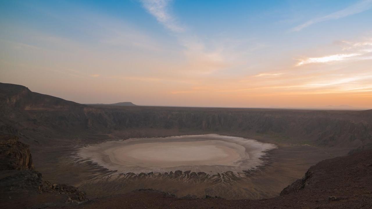 Hotel Dar Al Tawhid Intercontinental Makkah By Ihg Mekka Exterior foto The photo shows a large volcanic crater, characterized by its circular shape and steep walls. The interior appears dry with a light-colored base, possibly indicating a lakebed or sediment. Surrounding the crater, the landscape is rocky and barren, wi
