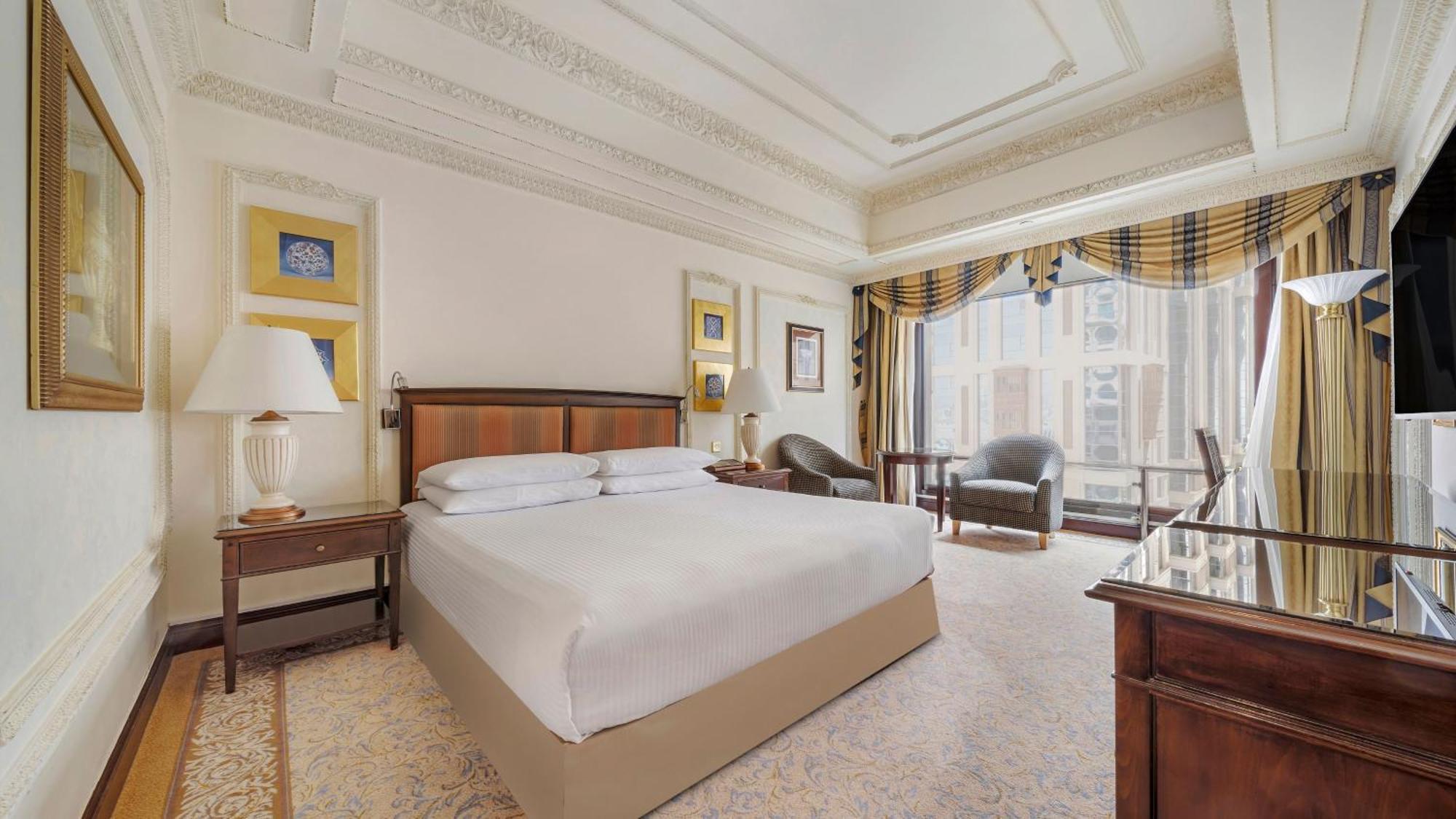 Hotel Dar Al Tawhid Intercontinental Makkah By Ihg Mekka Exterior foto The photo shows a luxurious hotel room. It features a large bed with white bedding positioned in the center. On either side of the bed are wooden nightstands with lamps. The room has elegant decor, including decorative framed artwork on the walls and