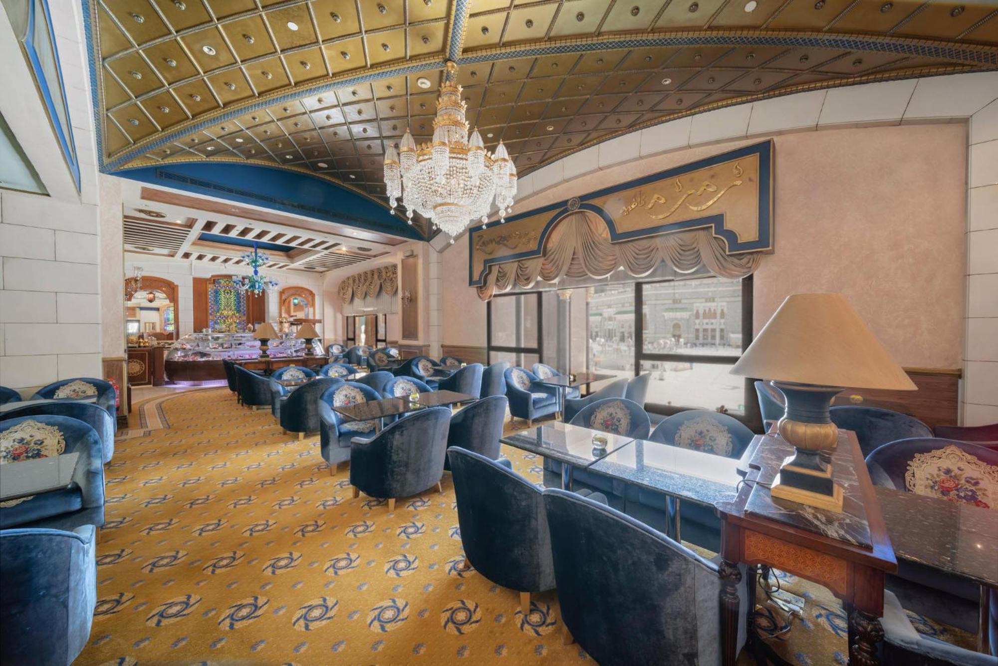 Hotel Dar Al Tawhid Intercontinental Makkah By Ihg Mekka Exterior foto The photo shows an elegant interior of a lounge or restaurant. The space features a high ceiling with a decorative design, highlighted by a chandelier hanging from it. The floor is covered in a patterned yellow carpet, and the room is furnished with 