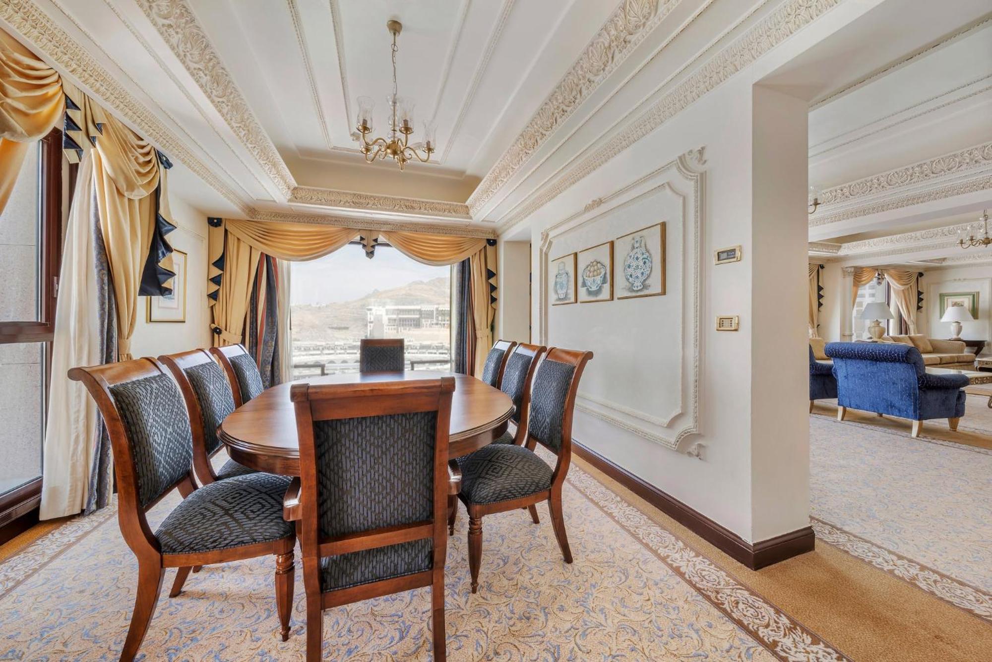 Hotel Dar Al Tawhid Intercontinental Makkah By Ihg Mekka Exterior foto The photo displays an elegant dining area featuring a wooden oval table surrounded by eight upholstered chairs. The decor includes rich curtains, with intricate detailing and a chandelier above the table. There are decorative wall frames with circula